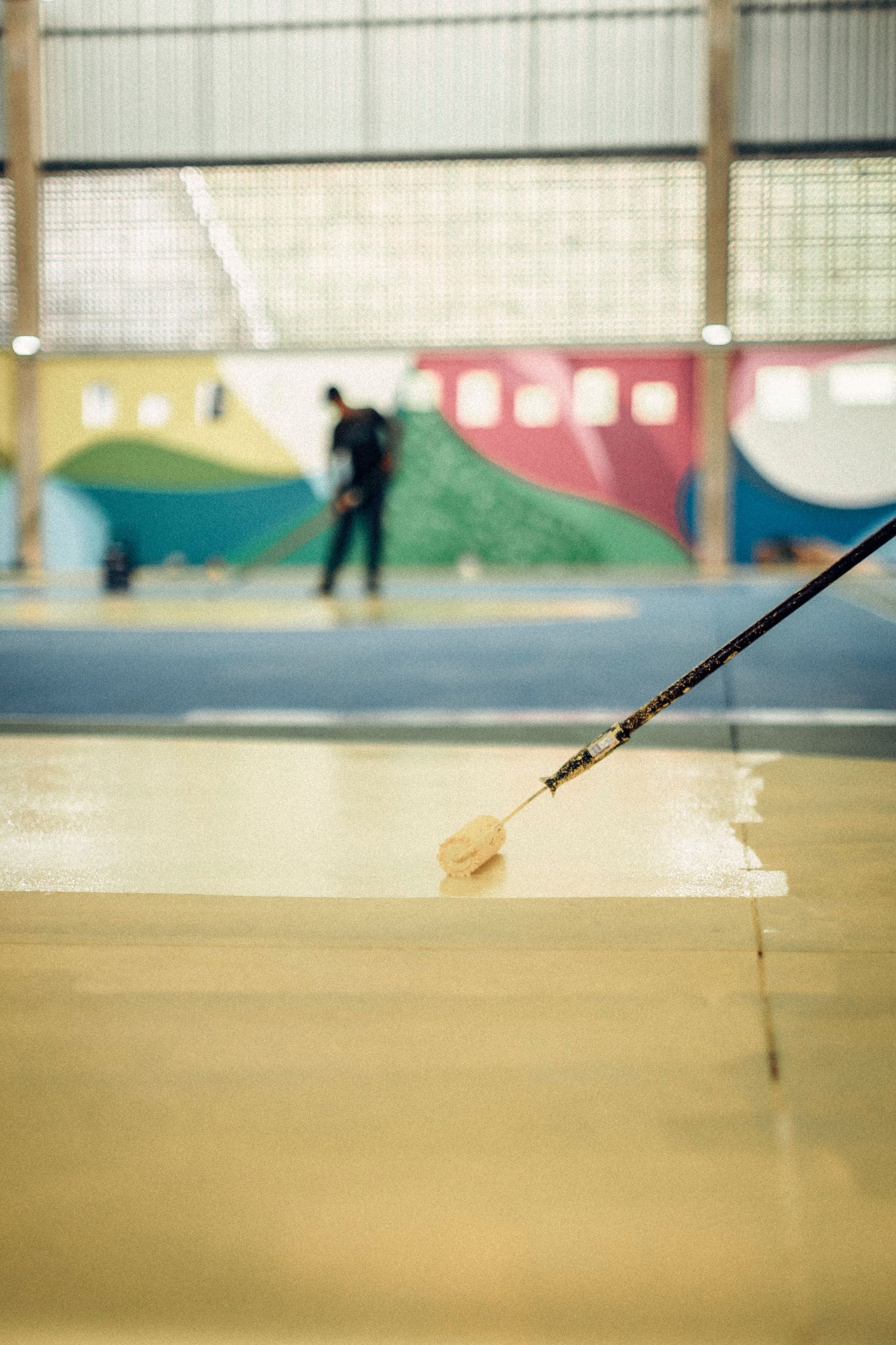 Man painting indoor sports hall floor with roller for renovation.
